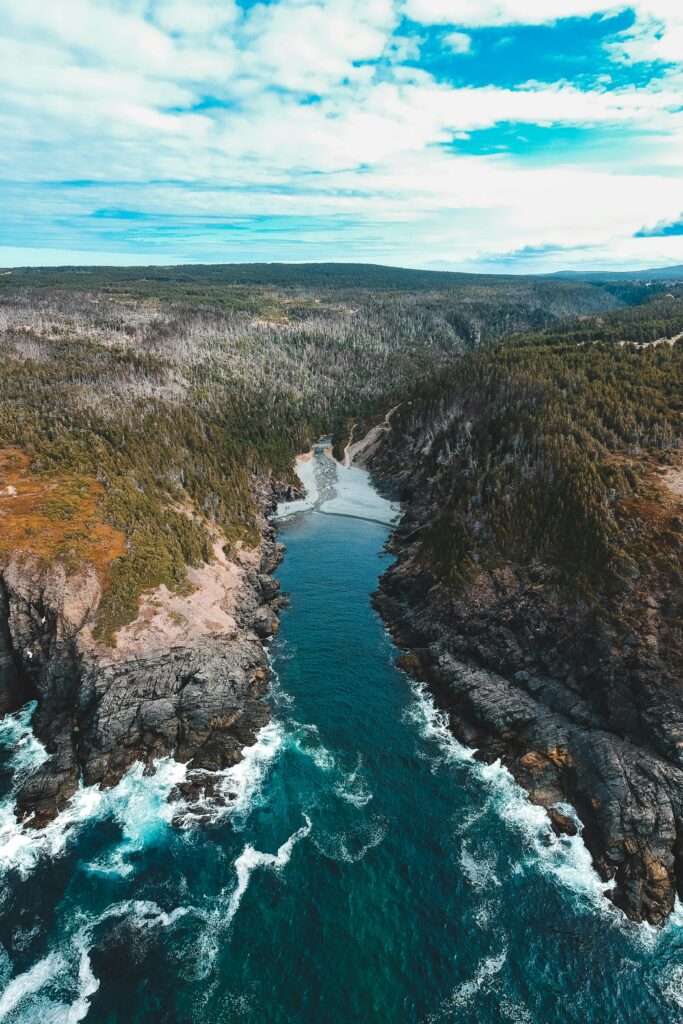 Drone view of small narrow blue sea bay surrounded with rough grassy shores under blue sky